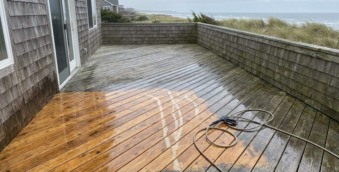 A weathered cedar deck being pressure washed, the foreground boards restored to warm honey wood beside still-gray boards.